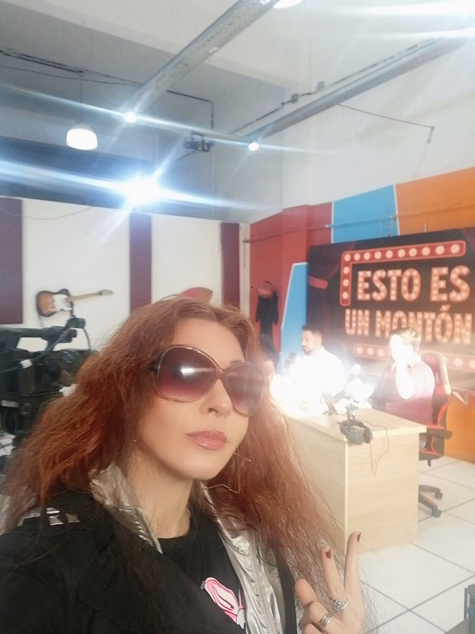 Eva ArtVision con anteojos de sol en un set de TV, con cámaras y escenografía de fondo