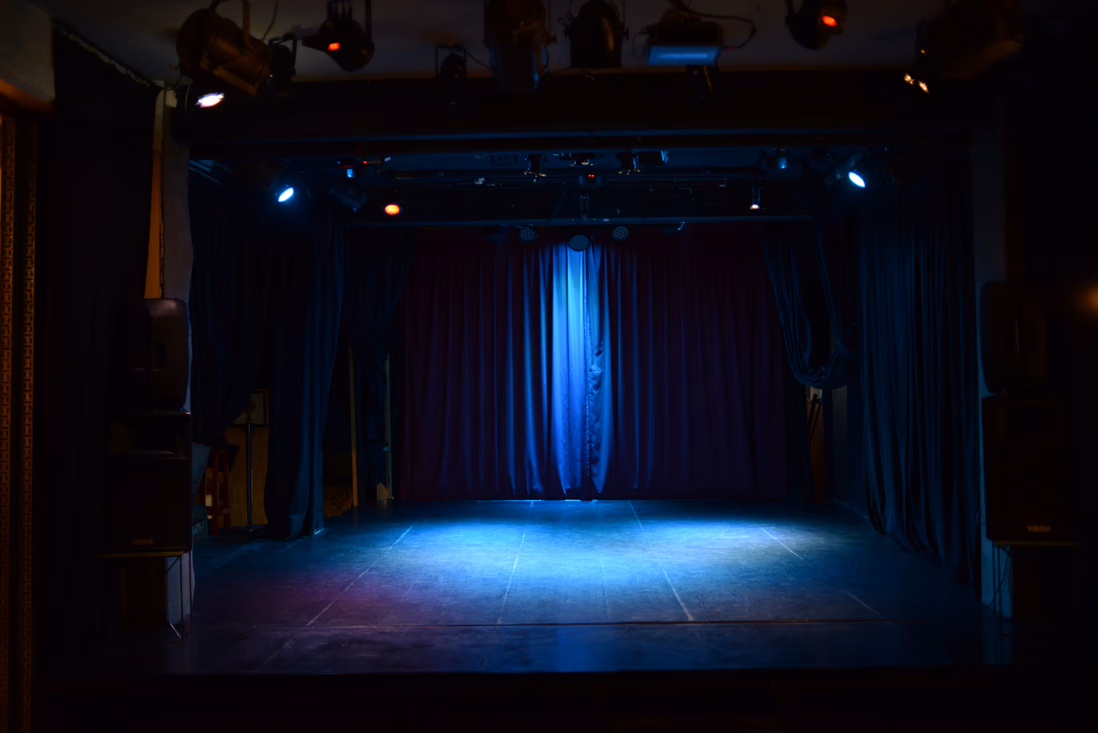 Escenario vacío con telones azules y luces de teatro encendidas, antes de la función