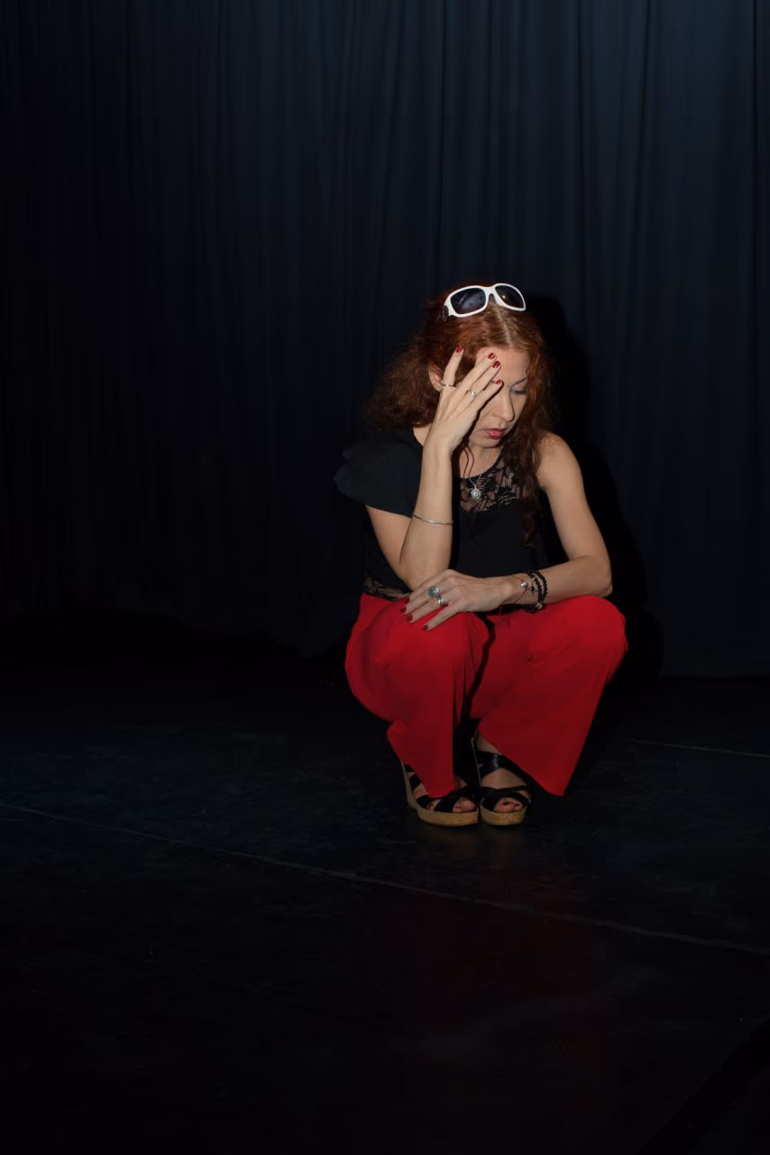Eva ArtVision agachada en escena, la mano en el rostro y anteojos sobre el pelo