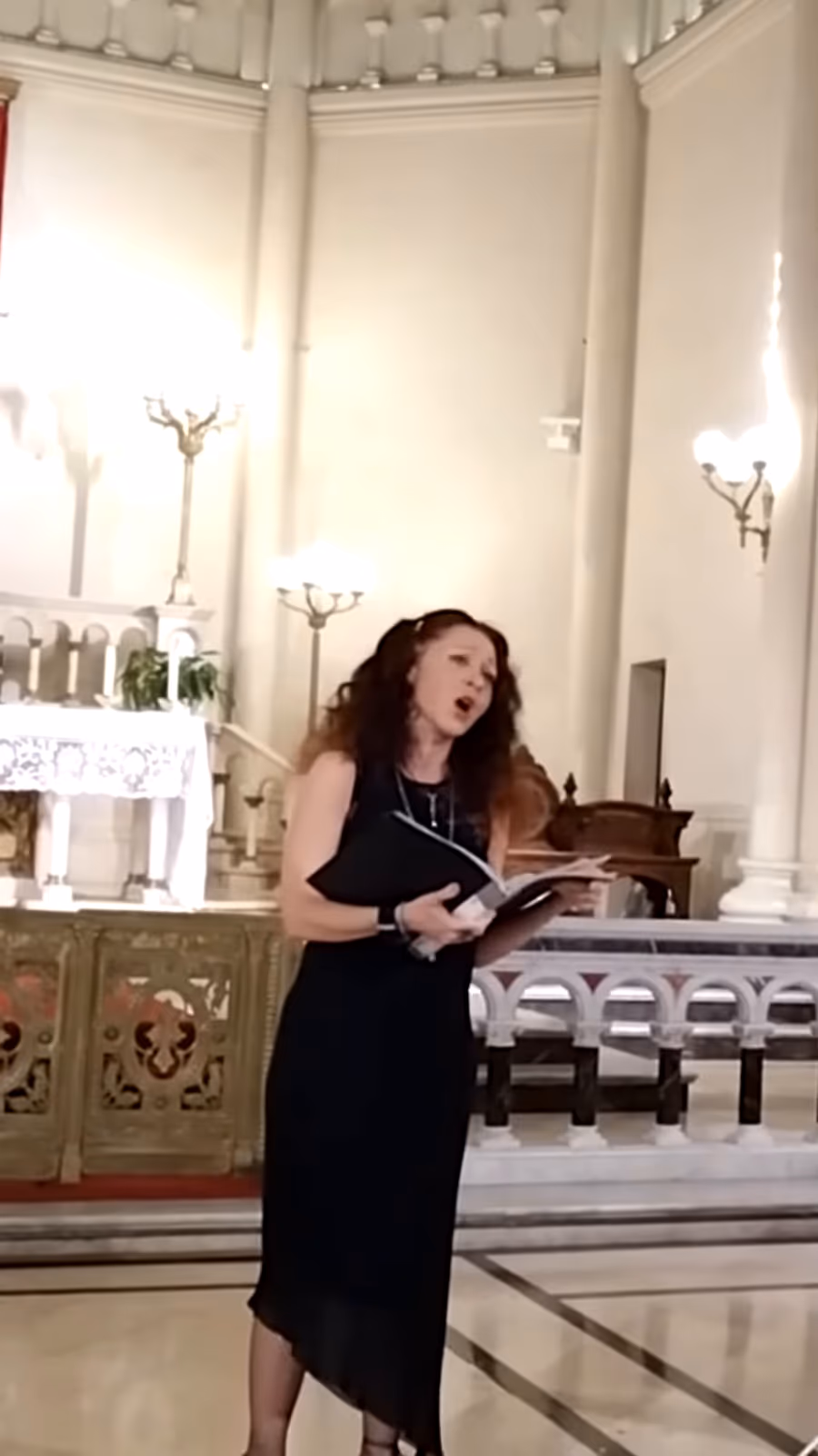 Eva McCat cantando en concierto, con vestido negro y la partitura en la mano, en una iglesia de Buenos Aires